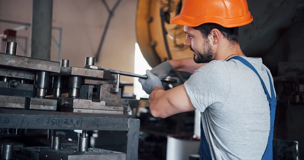 Portret młodego pracownika w kasku ochronnym na terenie dużej hali metalurgicznej.